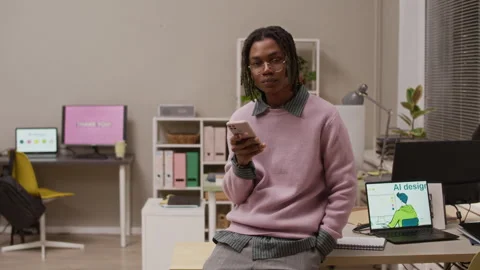 Portrait of African American Guy with Smartphone Leaning at Desk with Laptop Stock Footage 327768280