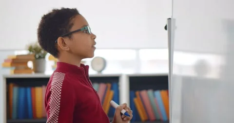 Portrait of african boy writing solution of sums on white board at school. Stock Footage 153420070