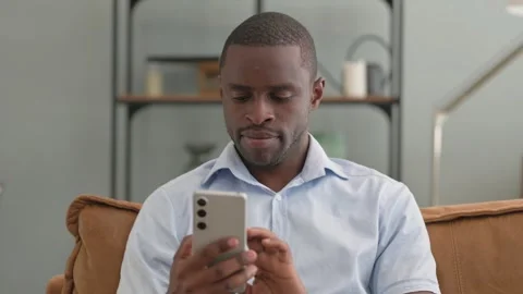 Portrait of African Man Text Messaging on Phone Sitting on Sofa at Home Stock Footage 287920499