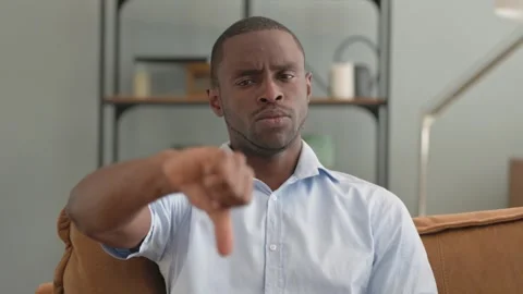 Portrait of African Man with Thumbs Down Sitting on Sofa at Home Stock Footage 287918562