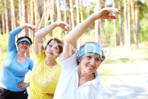 Portrait of aged women with their arms raised while doing physical exercise Stock Photos