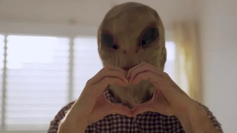 Portrait of alien faced man making a heart hand gesture to camera inside Stock Footage 316734695