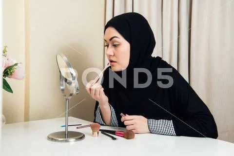 Portrait of an arab saudi woman painting her lips with a lipstick at home Stock Photos