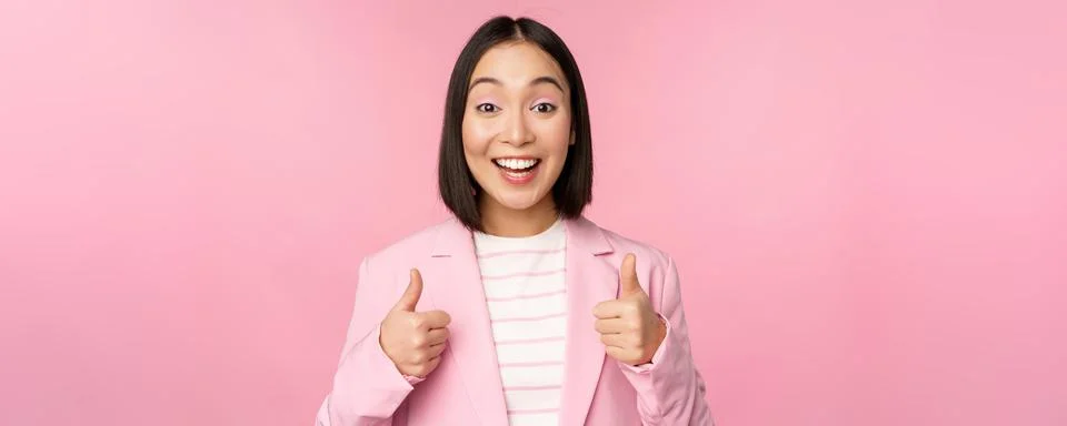 Portrait of asian businesswoman smiling satisfied, showing thumbs up, praise Stock Photos