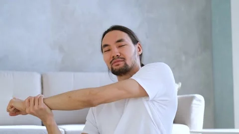Portrait asian man doing stretching while sitting on floor in living room Stock Footage 151874033
