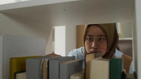 Portrait of Asian Muslim Student Selecting Book from Library Shelf Stock Footage 337472347