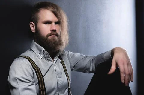 A portrait of an attractive brooding bearded man sitting against a wall looks in Stock Photos