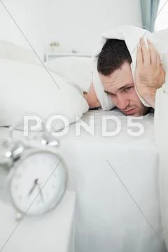Portrait of an attractive man covering his ears with a duvet while his alarm is Stock Photos
