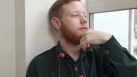Portrait of an attractive red-haired, bearded guy sitting on the windowsill. Stock Footage 294038935