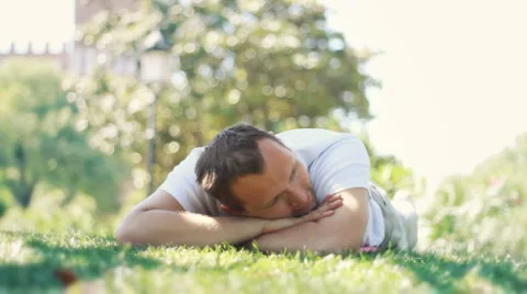 Portrait of attractive smiling man lying on green grass in park Stock Footage 6530539