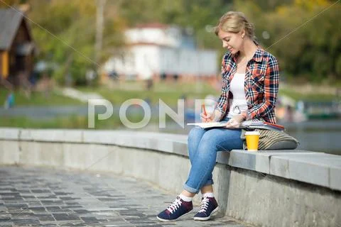 Portrait of an attractive student girl sitting at bridge writing Stock Photos