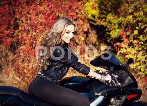 Portrait of an attractive young blond woman biker posing on her motorcycle. H Stock Photos