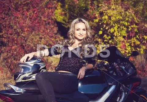 Portrait of an attractive young blond woman biker posing on her motorcycle. H Stock Photos