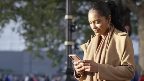 Portrait of attractive young female using her phone outdoors in the sunlight, in Stock Footage 252408201