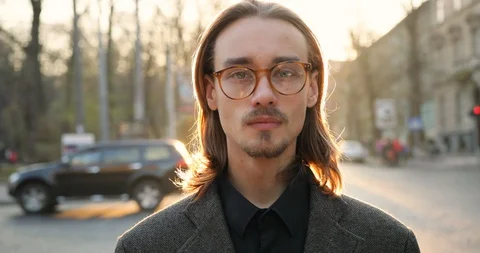 Portrait of attractive young man with long hair in glasses and jacket smiling Stock Footage 123770332