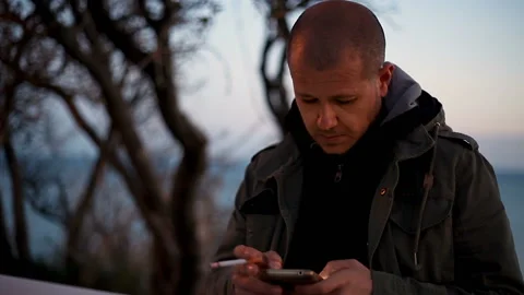Portrait of a bald young Man in a jacket smoking with a phone in his hands Vidéo 150226659