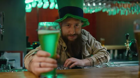 Portrait of Bearded Barman in Leprechaun Hat Serving Pint of Green Beer Stock Footage 261511367