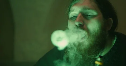 Portrait of bearded guy smoking vape and makes rings in the green smoke Stock Footage 88061237