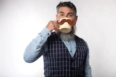 Portrait of bearded man drinking from a cup with a fake paper mustache on whi Stock Photos