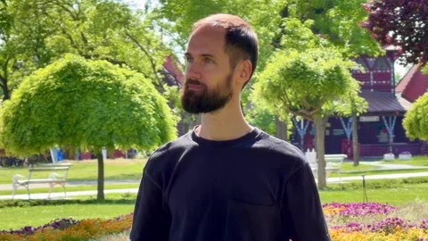 Portrait of Bearded Man Standing in Palic Park with Historic Building Background Vídeo Stock 336178229