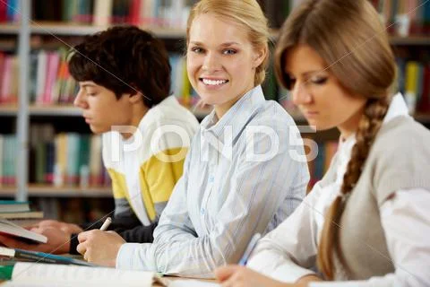 Portrait of beautiful blonde between two groupmates in college library Stock Photos