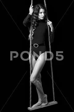 Portrait of beautiful caucasian model posing on rope swing in body dress on b Stock Photos