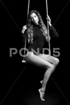 Portrait of beautiful caucasian model posing on rope swing in body dress on b Stock Photos