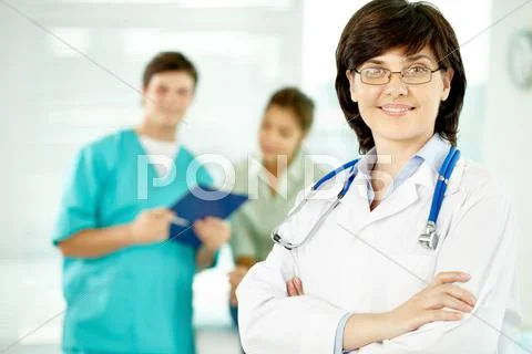 Portrait of beautiful female doctor looking at camera with her colleagues behind Stock Photos
