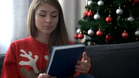 Portrait of beautiful woman wearing stylish christmas tree sweater and reading a Stock Footage