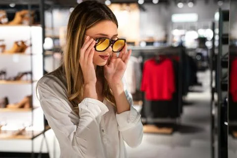 Portrait of beautiful young woman choosing sunglasses in store. Shopping people Stock Photos