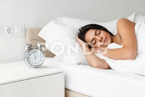 Portrait of beautiful young woman sleeping in bed at bedroom, with alarm cloc Stock Photos