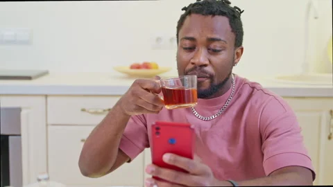 Portrait of black man with cup of tea and smartphone in home kitchen in weekend Stock Footage 262693904