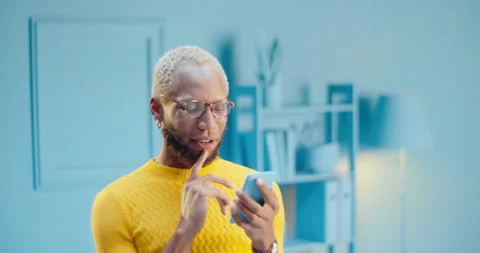 Portrait of a black man in spectacles using a mobile phone while thinking and Stock Footage 163146290