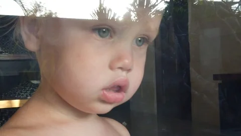 Portrait of blond brooding two-year-old boy standing behind the glass. Stock Footage 107965398