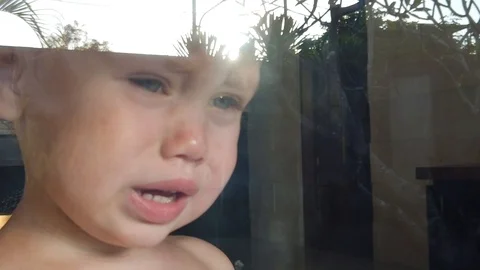  portrait of blond crying two-year-old boy standing behind the glass Stock Footage 107965230