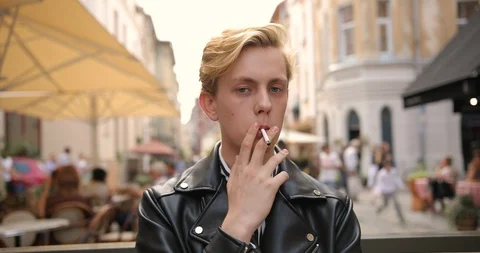 Portrait of a blond guy in a black jacket who smokes a cigarette on the street. Stock Footage 126575910