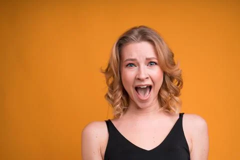 Portrait of a blonde girl with an open mouth laughing on an orange background Stock Photos