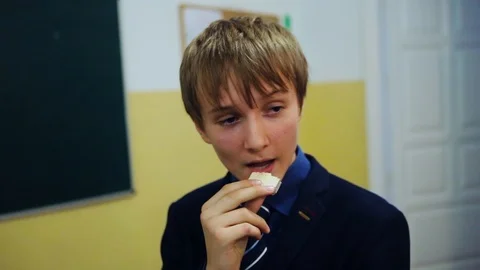 Portrait boy eats waffles at school background in classroom break meal child Video stock 99255575