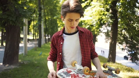 Portrait boy look at camera listens to music in headphones walk keeps skate in Stock Footage 92049343