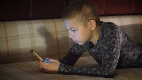 Portrait of a boy lying on a sofa and playing on a smartphone in vertical mode. Video stock 101028272