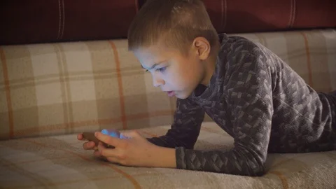 Portrait of a boy lying on a sofa and playing on a smartphone in horizontal mode Stock Footage 101028273