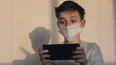 Portrait boy medical mask on face quarantine plays smartphone emotionally Stock Footage 127702353