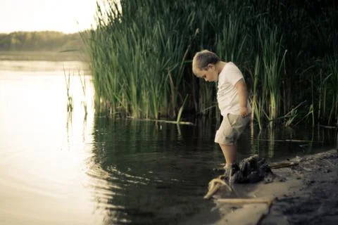 Portrait of boy testing the water of calm pond with leg Stock Photos