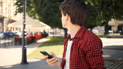 Portrait boy using mobile phone listens to music in headphones walk keeps skate Stock Footage 92051106