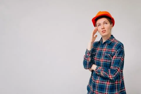 Portrait of a brooding girl builder in uniform in an orange helmet against a  Stock Photos