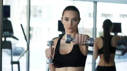 Portrait of brunette with slender physique doing exercises using dumbbells. One Video stock 199490660