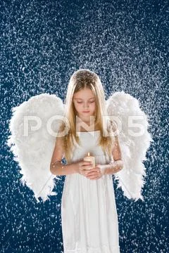 Portrait of calm girl wearing angel wings and holding candle in flurry snowfall Stock Photos