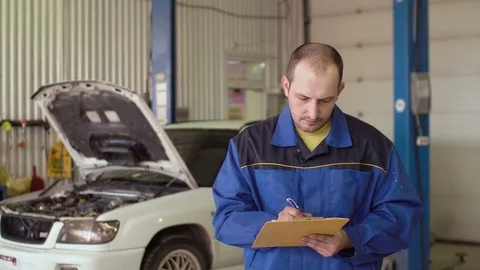 Portrait of a car mechanic writing in a note pad clipboard behind car with Stock Footage 74625172