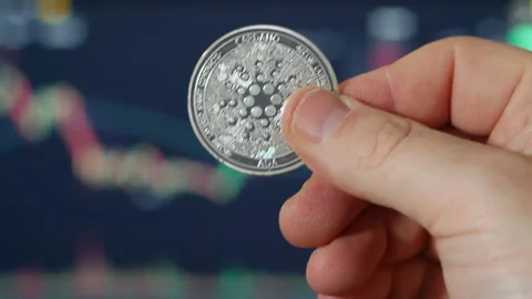 A portrait of Cardano ADA silver coin being held in hand with trading Stock Footage 160949744