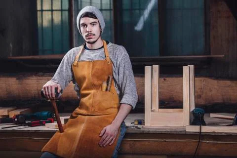 Portrait of carpenter holding hammer while sitting on bench at workshop Stock Photos